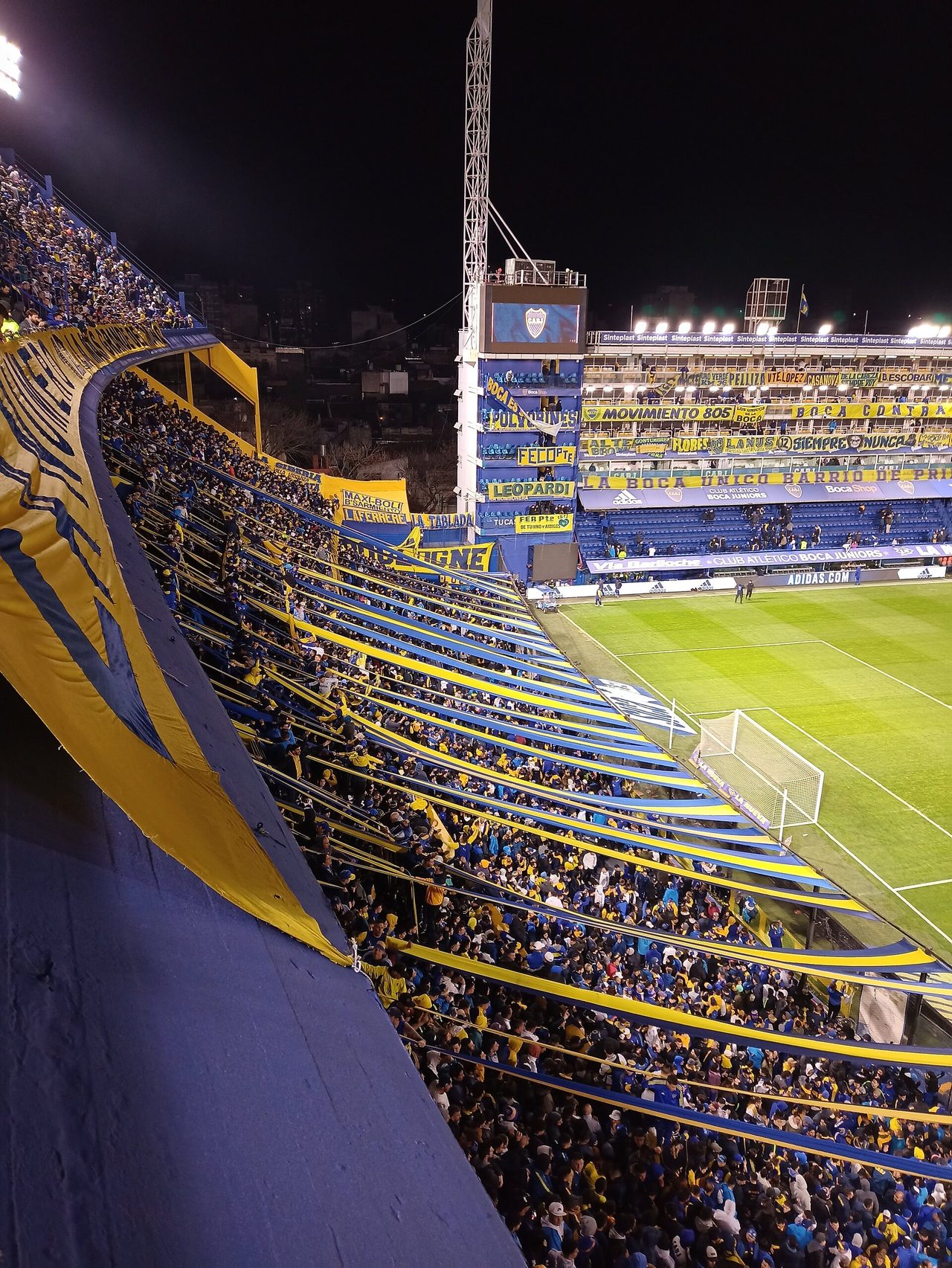 La Bombonera de noche con la tribuna de Boca Juniors repleta y el césped verde del campo a la derecha